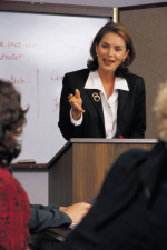Photograph of a woman at a lectern, speaking to a group of people